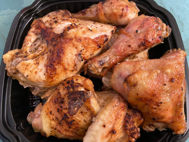 A platter of cooked chicken pieces, including thighs and drumsticks, presented in a black takeout container.