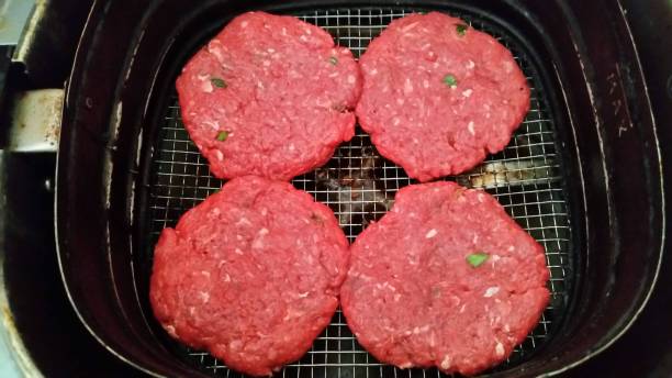 Four raw beef patties placed on a wire rack in an air fryer basket