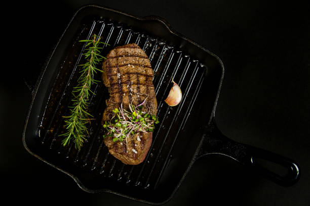 Grilled steak on a black cast iron grill pan with herbs and garlic