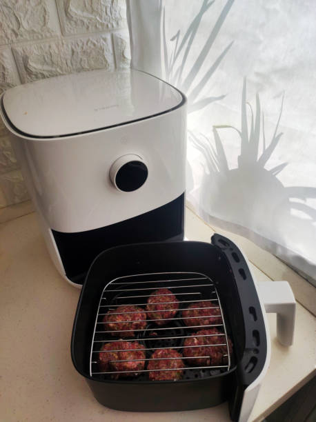 An air fryer with a basket containing meatballs placed on a countertop next to a window.