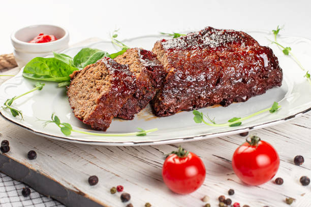 A plate of meatloaf garnished with spinach and served with a side of ketchup, accompanied by cherry tomatoes and peppercorns.