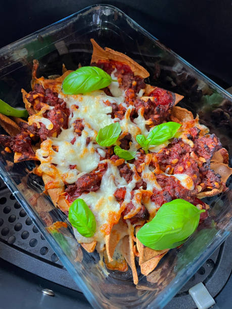 A glass dish filled with nachos topped with melted cheese, ground meat, and fresh basil leaves.