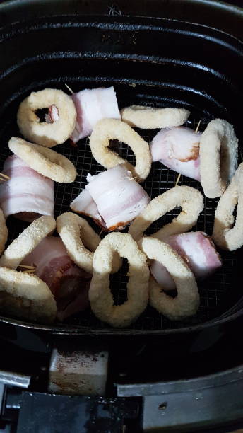 An air fryer basket filled with pieces of bacon-wrapped onion rings and battered rings.