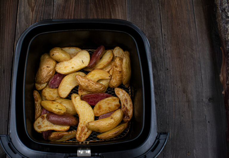 Air fryer filled with golden-brown potato wedges on a wooden surface.