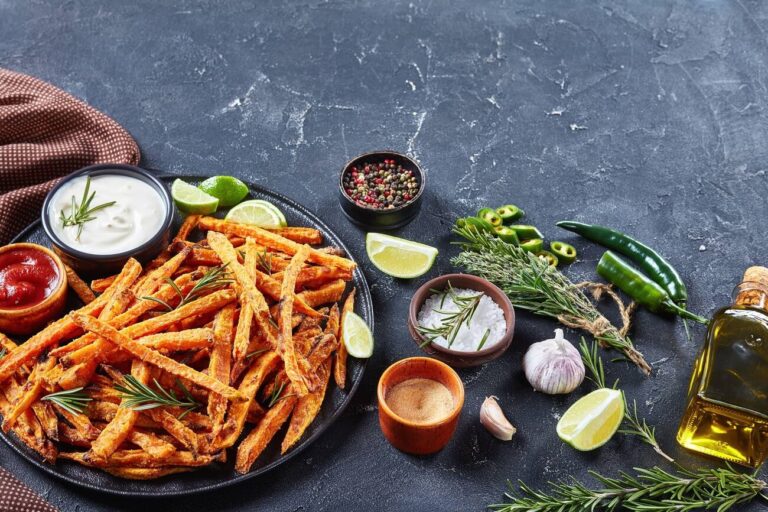 A plate of crispy sweet potato fries garnished with rosemary, served alongside dipping sauces and fresh ingredients.