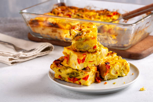 A plate of vegetable frittata squares with colorful peppers, stacked in front of a baking dish filled with frittata.