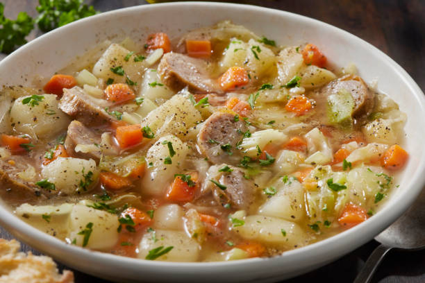 A warm bowl of hearty vegetable and meat stew featuring chunks of potatoes, carrots, and pieces of meat, garnished with parsley.