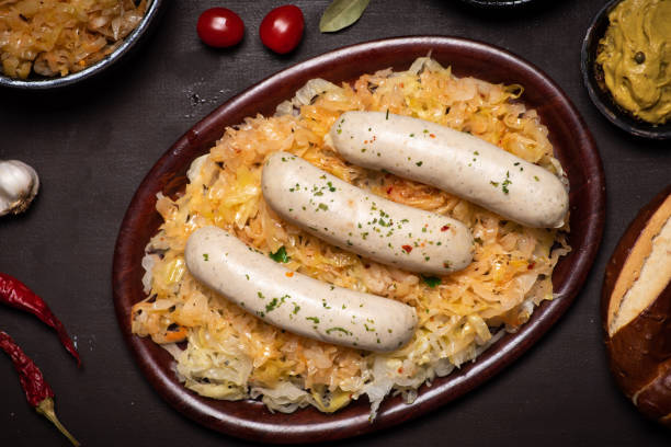 A serving of white sausages on a bed of sauerkraut, accompanied by cherry tomatoes and other garnishes.