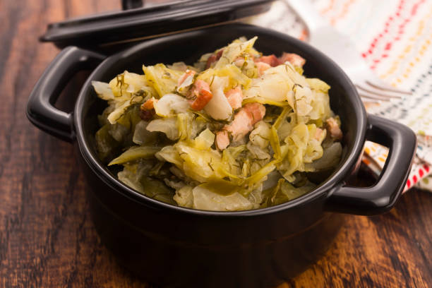 A black pot filled with cooked greens and meat on a wooden surface.