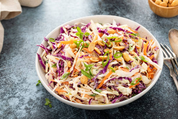 A colorful bowl of coleslaw with purple and green cabbage, carrots, and peanuts.