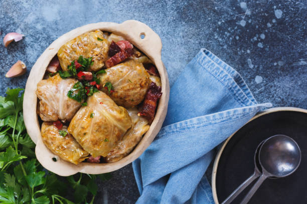 A dish of stuffed cabbage rolls garnished with parsley, surrounded by garlic cloves and a blue cloth napkin.