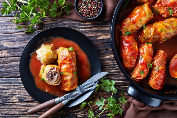 A plate of stuffed cabbage rolls with a pot of additional rolls in tomato sauce, garnished with parsley.