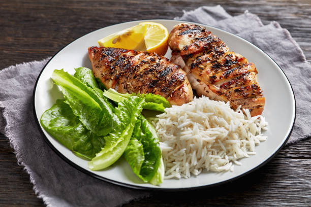 Grilled chicken breast served with lettuce, rice, and lemon on a white plate