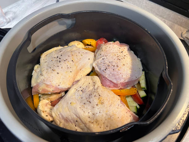 Cooked chicken thighs seasoned with pepper on a bed of colorful vegetables in a cooking pot.