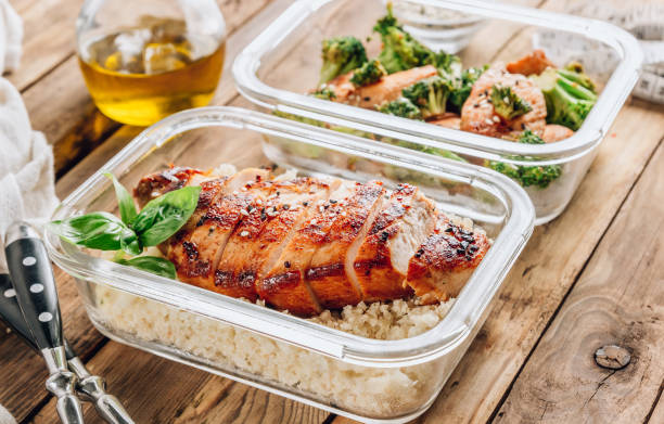 Two glass meal prep containers with cooked chicken and broccoli on a wooden table.