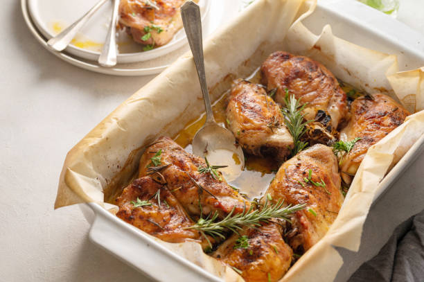 Baked chicken thighs garnished with fresh rosemary in a white baking dish.