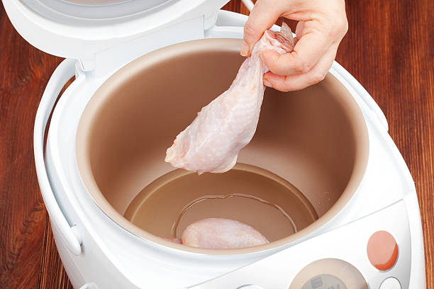 A hand holding a piece of chicken being placed into a multi-cooker.