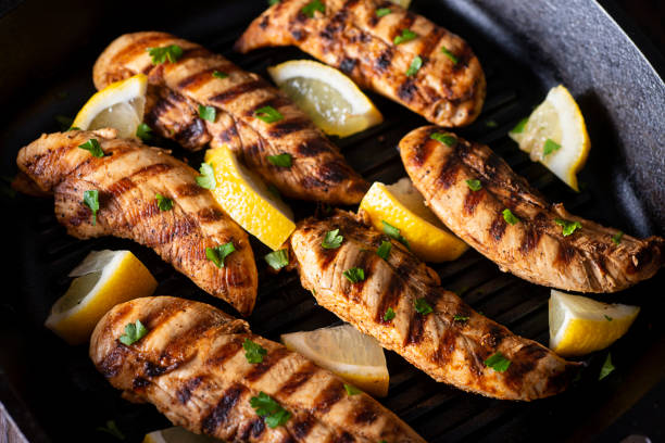 Grilled chicken breasts with lemon wedges on a black grill pan