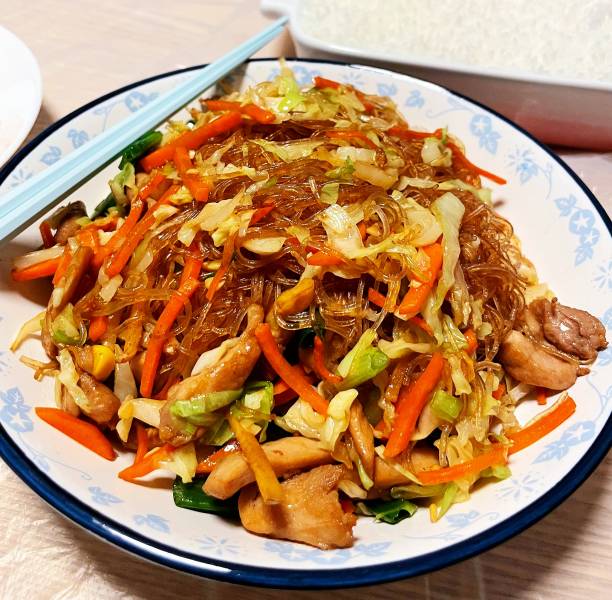 A colorful plate of stir-fried glass noodles with vegetables and chicken.