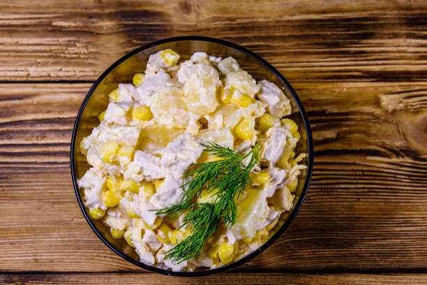 A bowl of salad with chicken, corn, and a garnish of dill on a wooden surface.