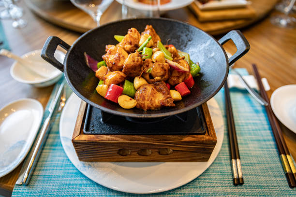 A sizzling dish of colorful vegetables and protein served in a black wok on a wooden base.