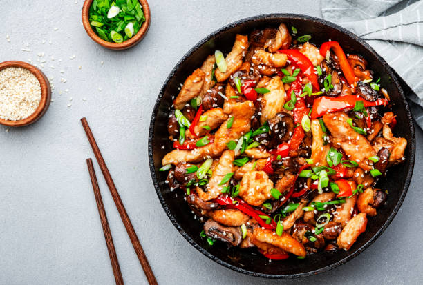 A colorful stir-fried chicken dish with red peppers and green onions in a black skillet.