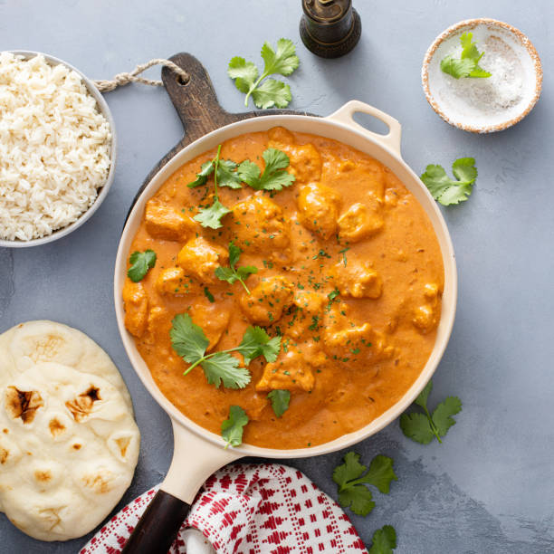 A plate of creamy chicken curry with rice and naan bread on a table.