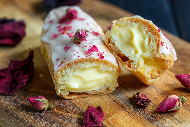 A delicious pastry filled with cream and topped with icing and rose petals on a wooden surface.