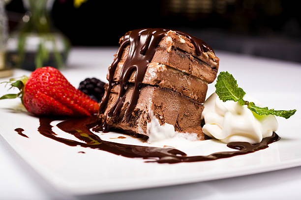 A tempting chocolate dessert slice topped with chocolate sauce, served with strawberries, blackberries, and whipped cream on a white plate.