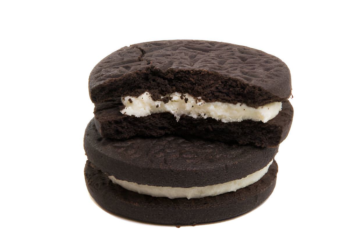 A close-up view of two stacked chocolate sandwich cookies with a cream filling, showing a broken top cookie revealing the white filling inside.