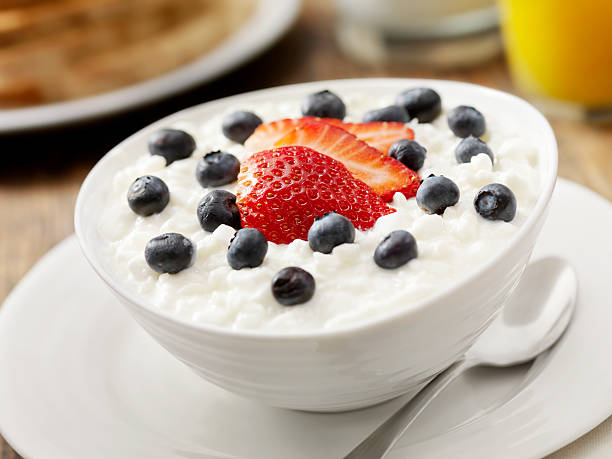 A bowl of cottage cheese topped with strawberries and blueberries, served on a white plate with a spoon.