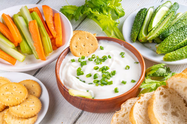 A bowl of creamy dip with chopped green onions, surrounded by fresh vegetables and crackers.