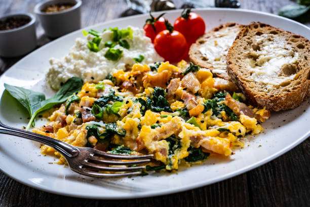 A close-up shot of a plate featuring scrambled eggs with spinach and ham, served with cottage cheese, sliced tomatoes, and toasted bread.