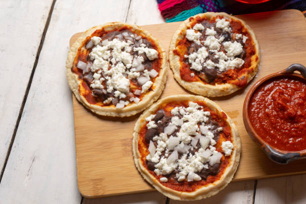 Three pizzas topped with cheese and meat on a wooden cutting board with a bowl of sauce