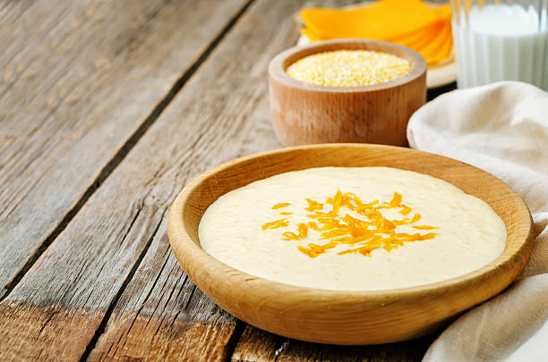 A wooden bowl filled with creamy cheese dip, topped with shredded cheese, next to ingredients on a rustic wooden surface.