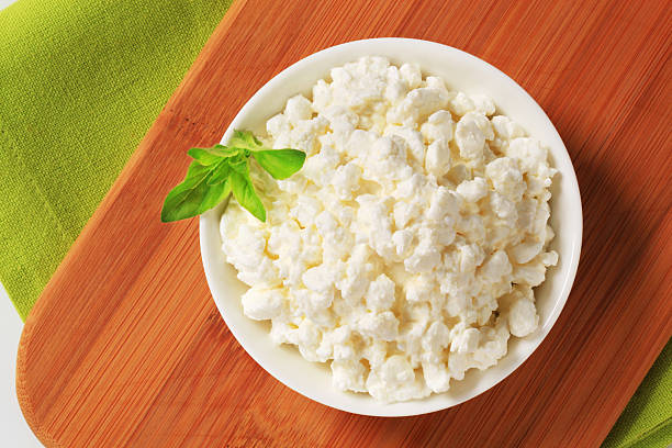 A bowl of fresh cottage cheese garnished with a sprig of basil on a wooden surface.