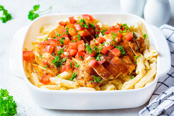 Baked chicken over creamy pasta topped with diced tomatoes and parsley in a white serving dish.