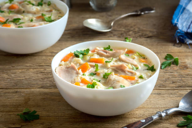 A bowl of creamy chicken soup with vegetables on a wooden table.