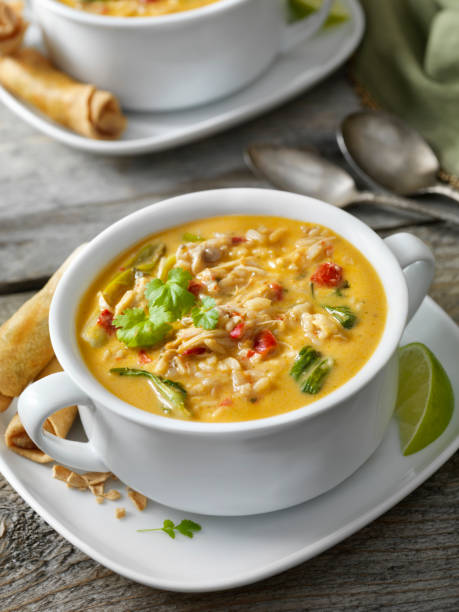 A bowl of creamy chicken soup garnished with cilantro, served with spring rolls and lime slices.