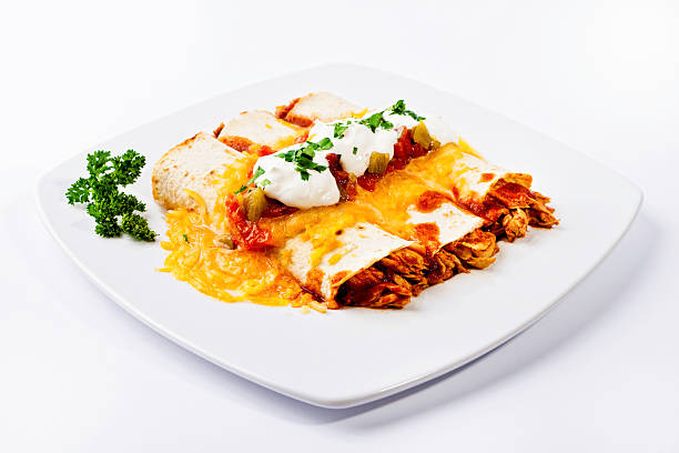 A plate of enchiladas covered in cheese and sauce with a side of sour cream and parsley.