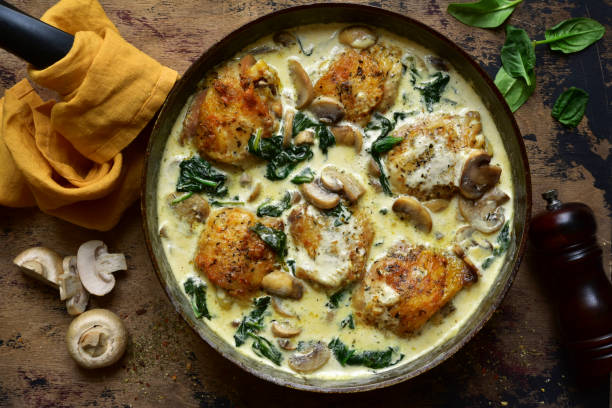 A creamy chicken dish with spinach and mushrooms in a skillet, accompanied by a yellow napkin and sliced mushrooms.