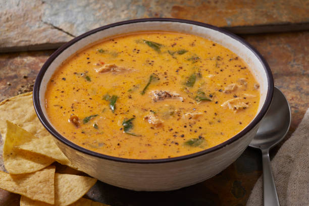 A bowl of creamy soup with chunks of chicken and spinach, served with tortilla chips on the side.