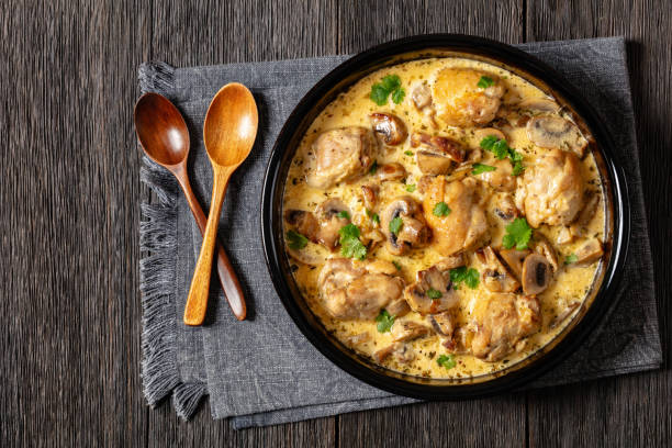 A bowl of creamy chicken with mushrooms garnished with fresh herbs, served on a dark wooden table.