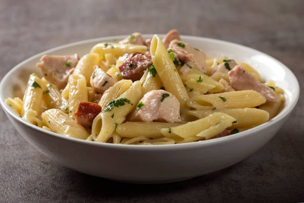 A bowl of creamy chicken pasta with penne and herbs, served on a textured surface.