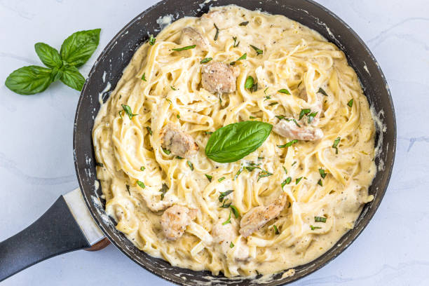 Creamy fettuccine pasta with chicken in a skillet, garnished with fresh basil leaves.