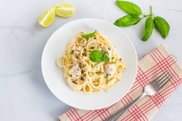 A plate of spaghetti with creamy sauce, garnished with basil leaves, served with lime wedges.