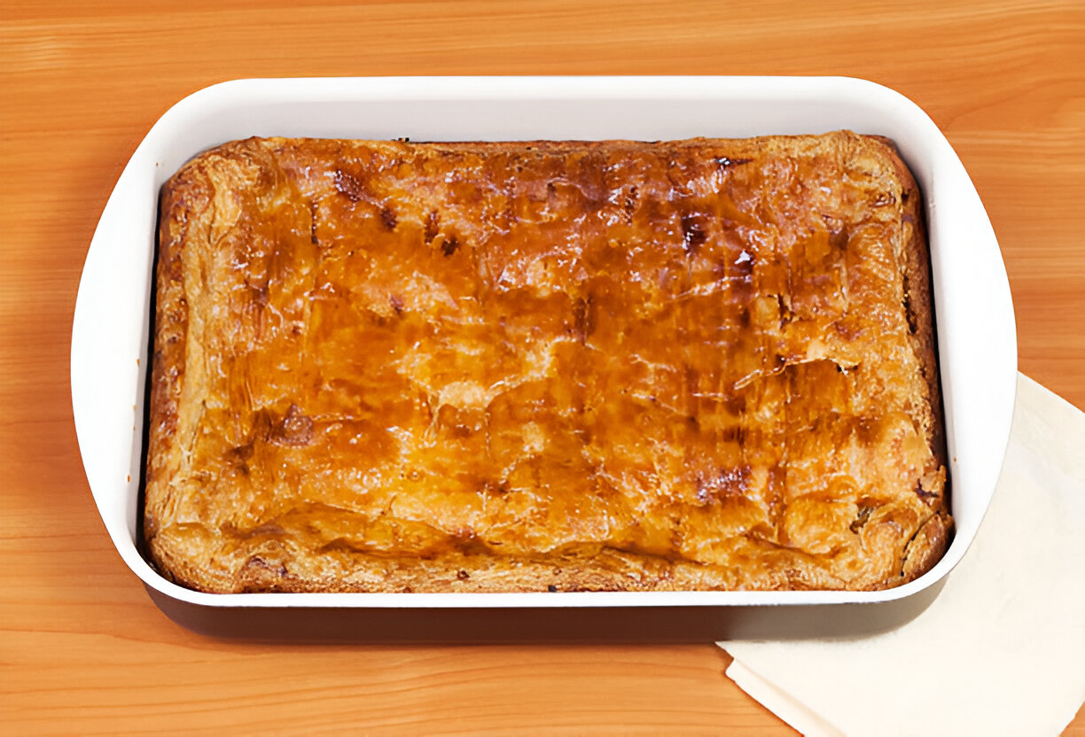 A golden-brown baked dish in a white rectangular dish resting on a wooden surface.