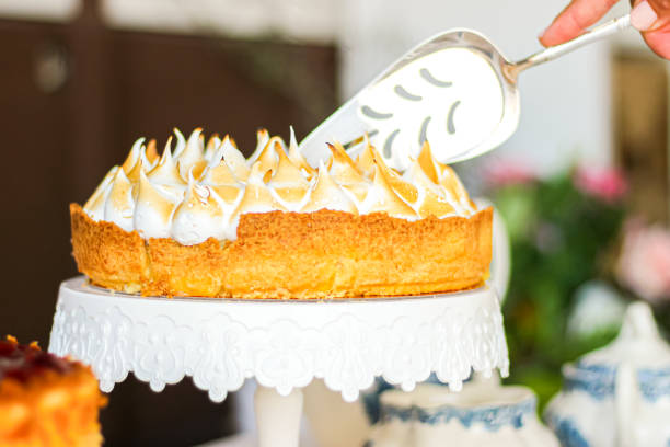 A hand using a serving spatula to cut a meringue-topped cake on a decorative cake stand.