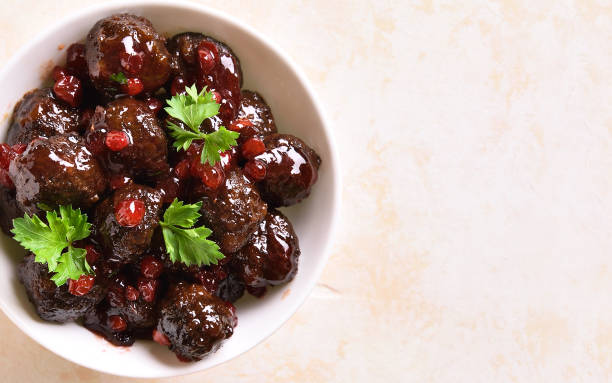 A bowl of meatballs drizzled with a sweet sauce and topped with cilantro and red berries.