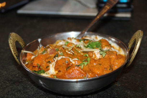 A bowl of rich, creamy Indian curry with garnish, served with a spoon.